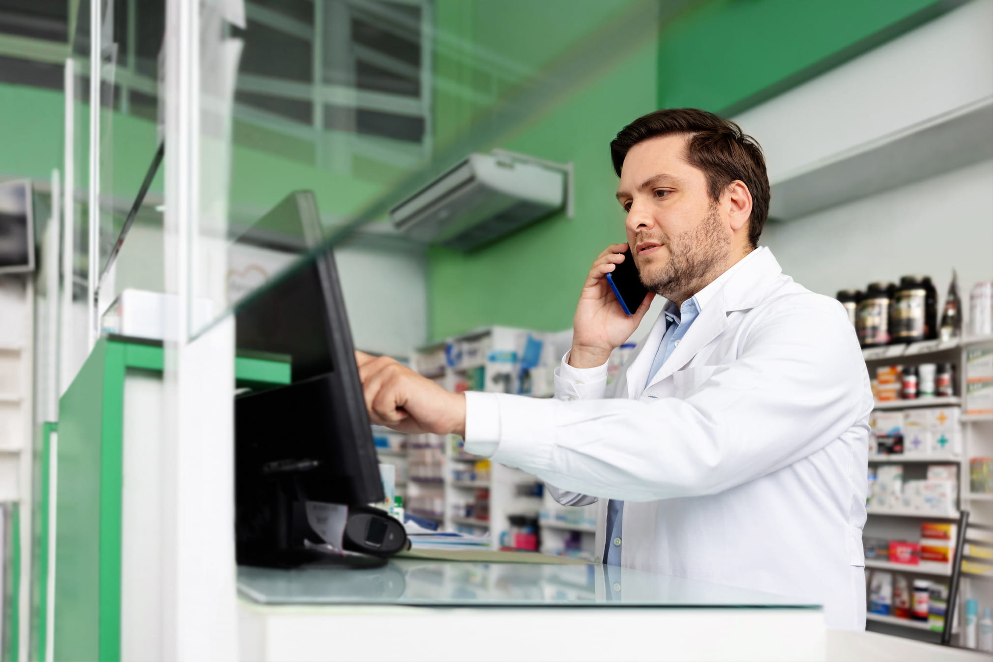 Pharmacist looking at the desctop while speaking on the phone