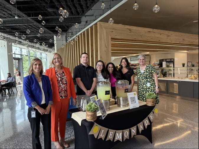 Group of people standing behind a lemonade stand.