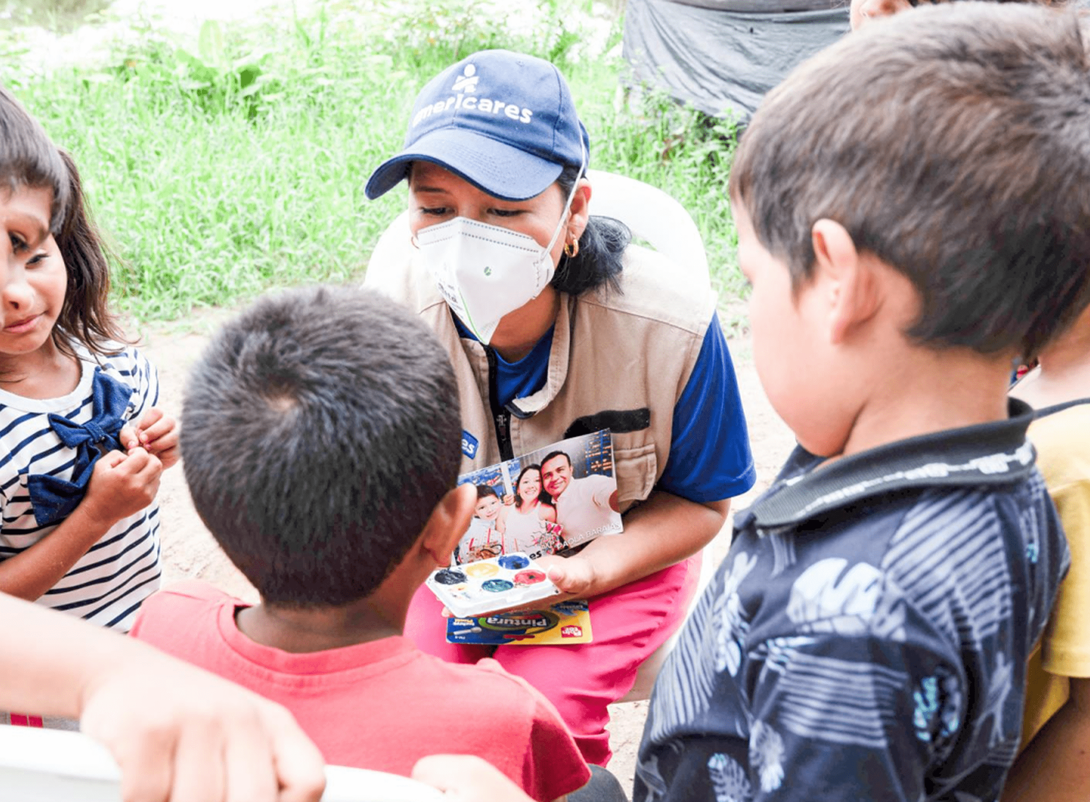 Three children surrounding a woman, who is painting their faces.