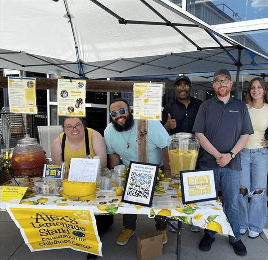 Smiling group of people standing close to a lemonade stand.