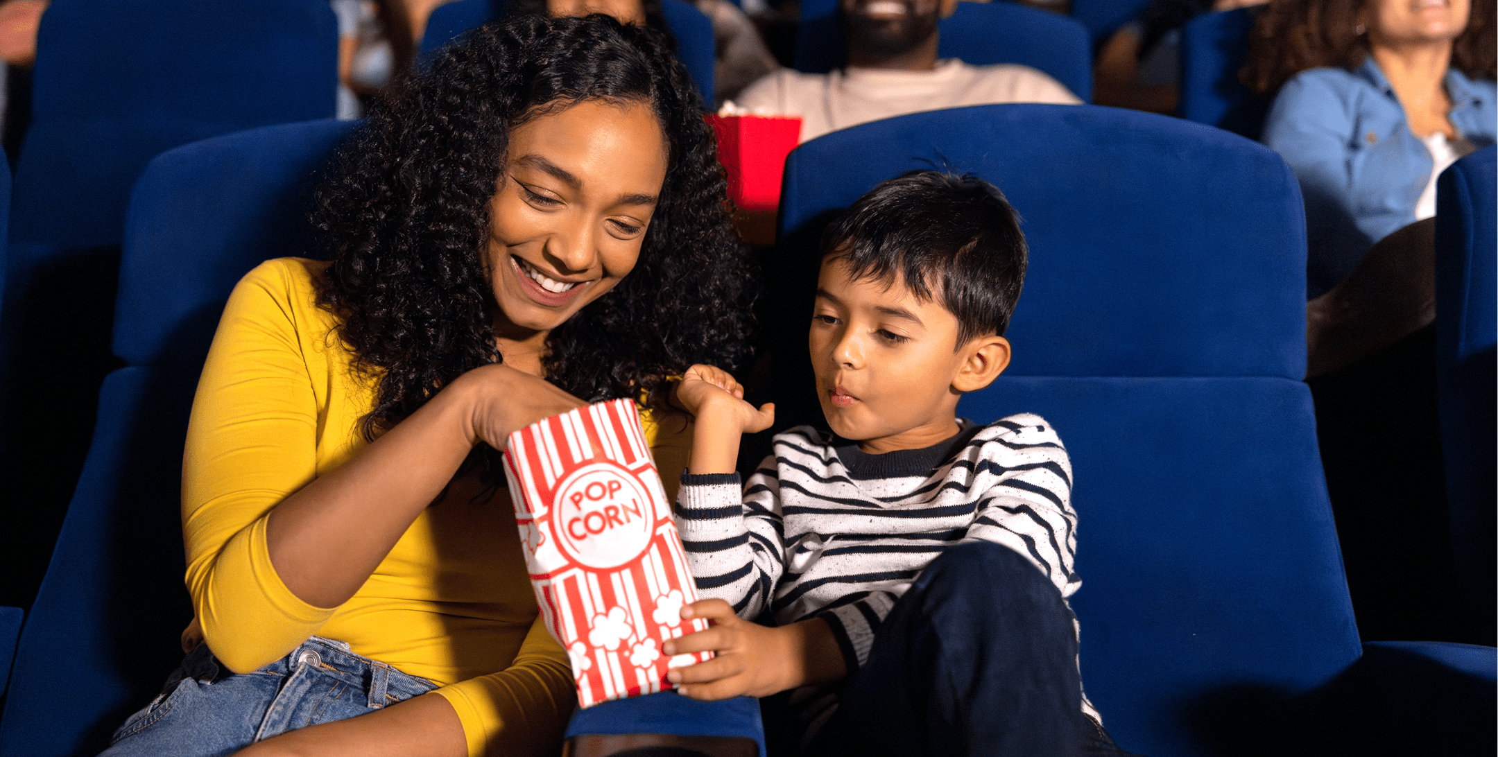 Young mom and son enjoying popcorn at a cinema.