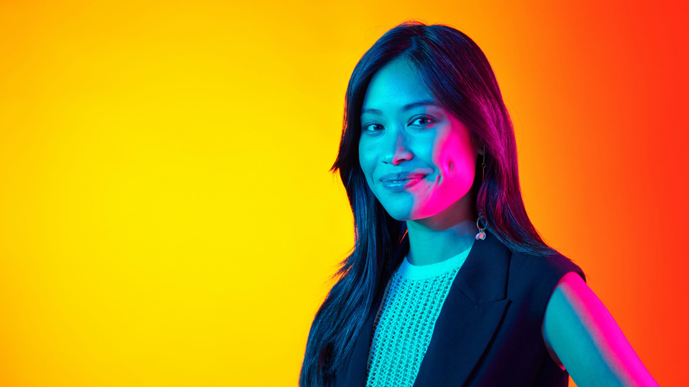 Donna che sorride alla fotocamera su uno sfondo arancione e giallo. Il suo viso è illuminato da luci blu e magenta.