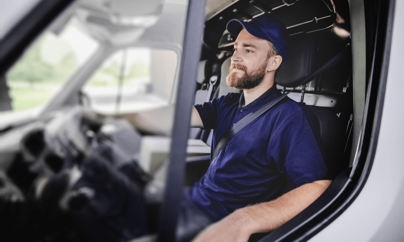 A delivery driver wearing a baseball cap sits in his van.