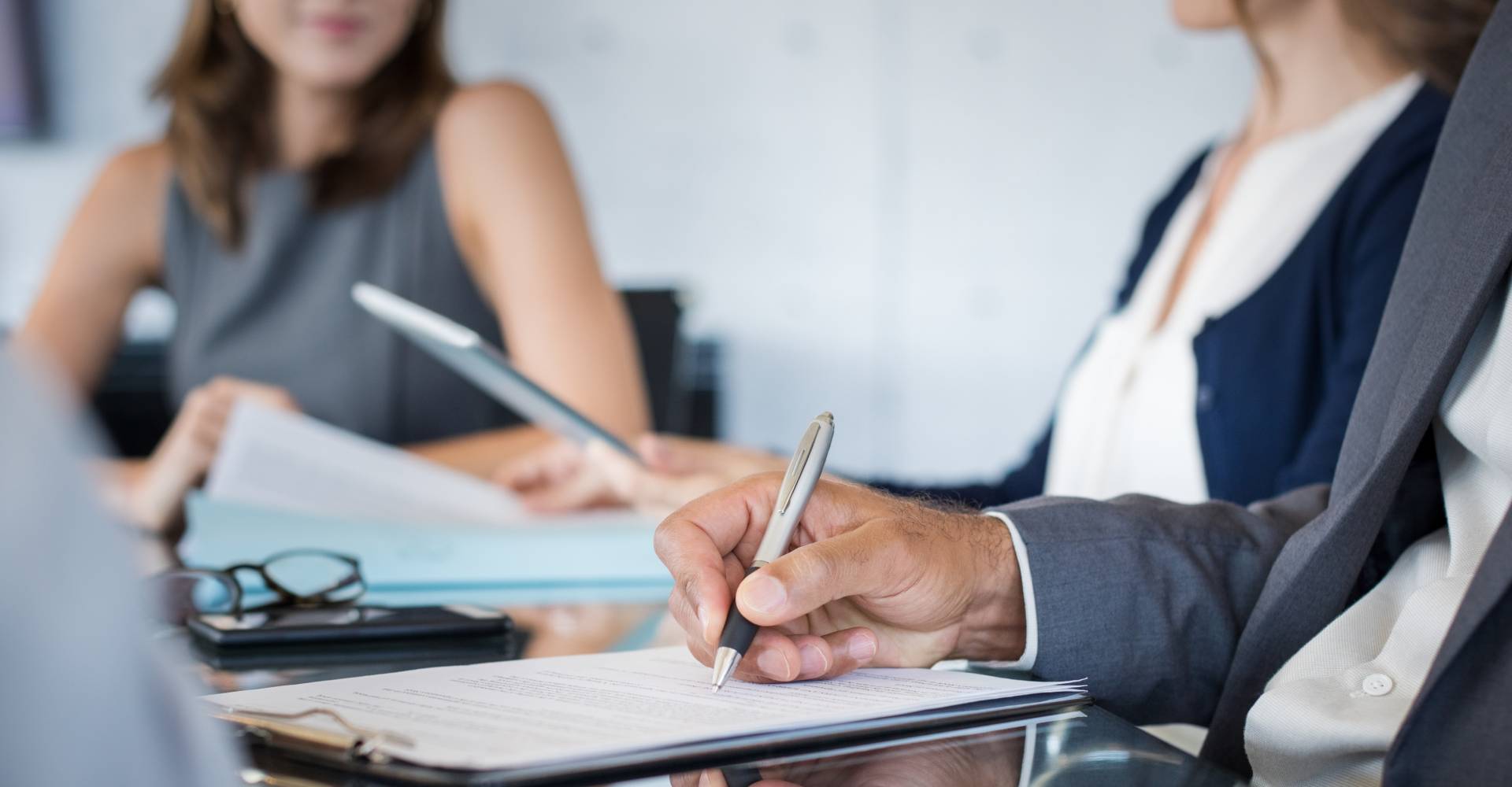 Closeup of hand of businessman holding pen and analyzing report during board meeting. Business people writing on document during annual meeting. Detail hand of business man fill the business contract.